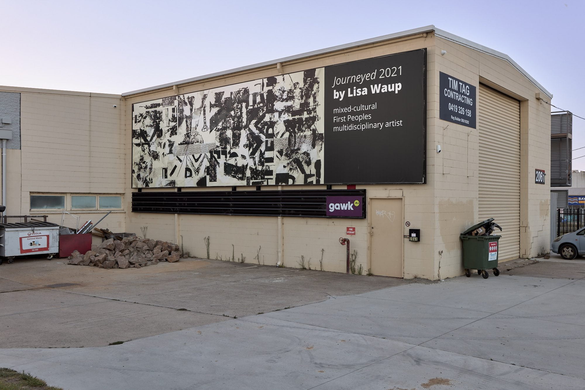 Image Description: A billboard filled collaged unintelligible black text and shapes on an off-white background.  The billboard is installed the side of a building.
