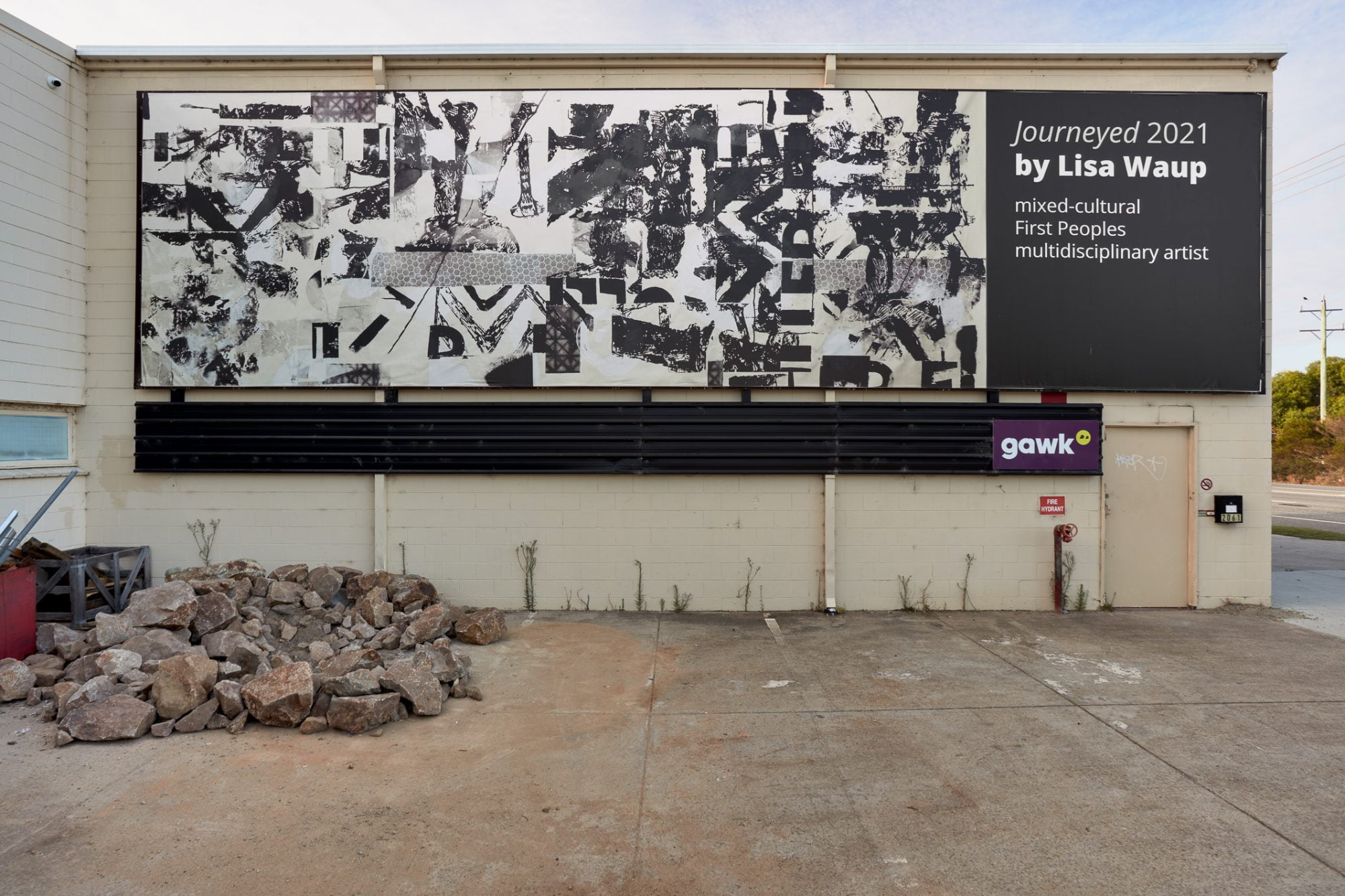 Image Description: A billboard filled collaged unintelligible black text and shapes on an off-white background.  The billboard is installed the side of a building.